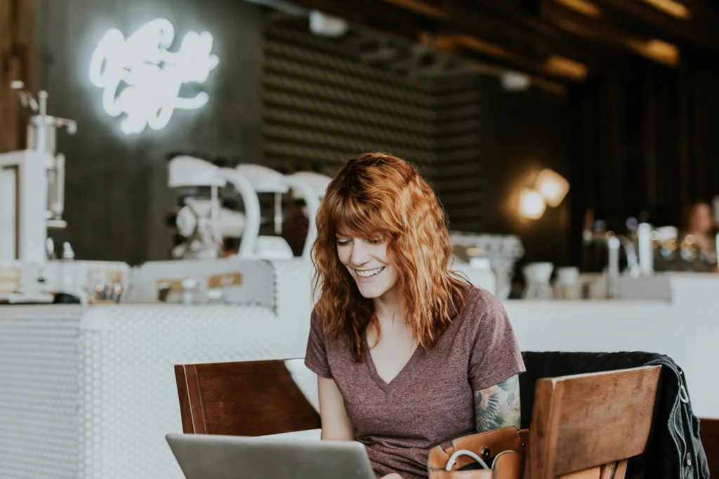 woman sitting on brown wooden chair while using silver laptop computer in room - 11society.com