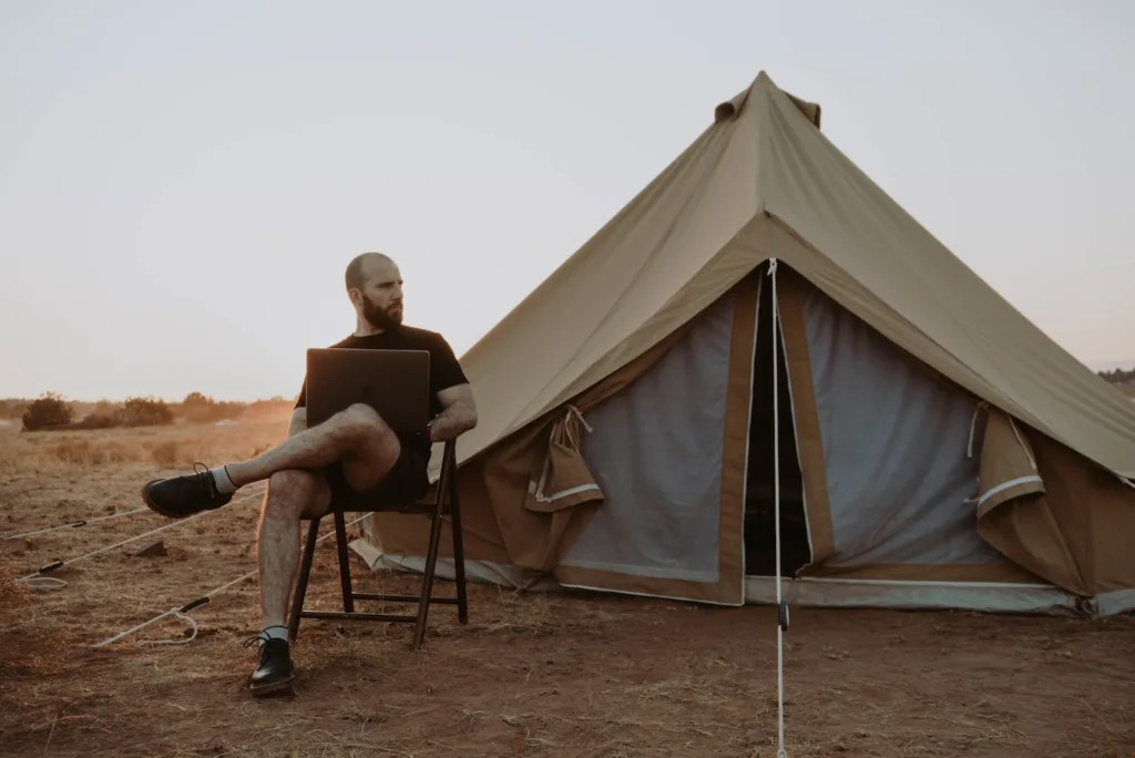 Man relaxing with laptop near tent