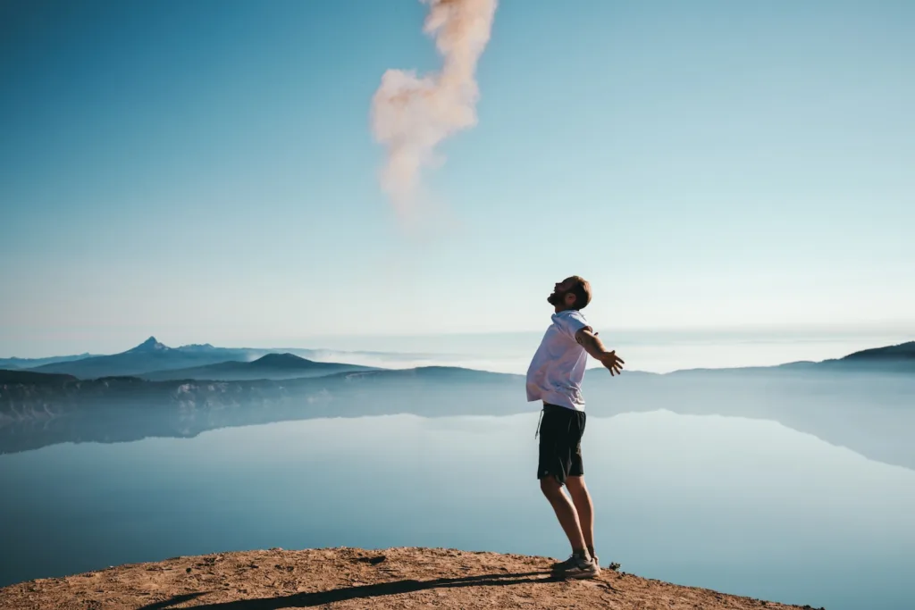 Financial freedom - man standing on sand while spreading arms beside calm body of water