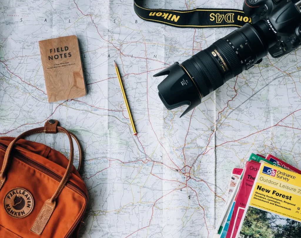 Travel Hacks - flat lay photography of camera, book, and bag